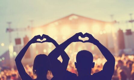 Two fans at a concert holding their hands up in the shape of a heart.